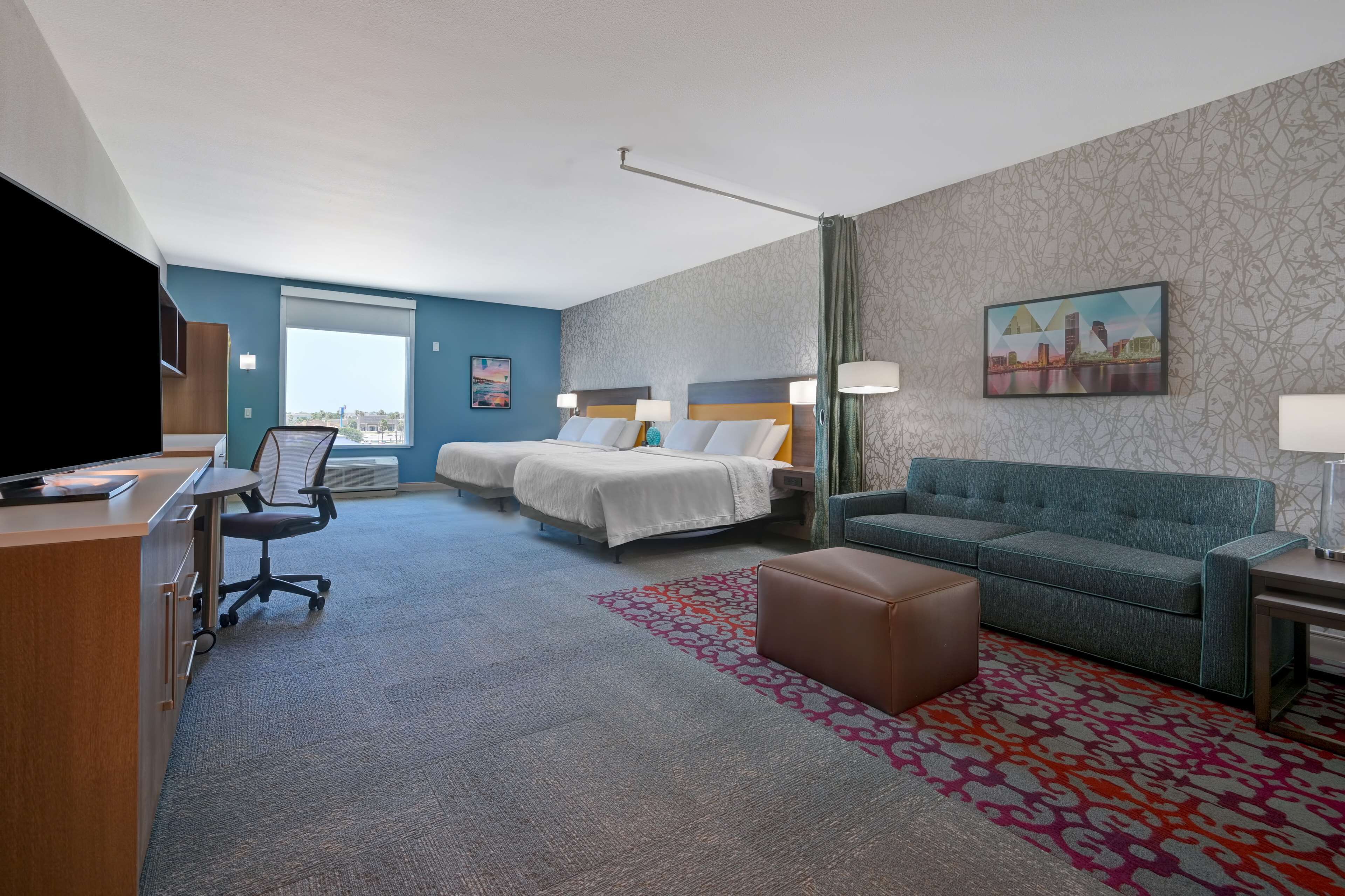 A hotel room with a desk, two beds, a sofa, and a TV.