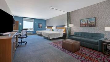 A hotel room with a desk, two beds, a sofa, and a TV.