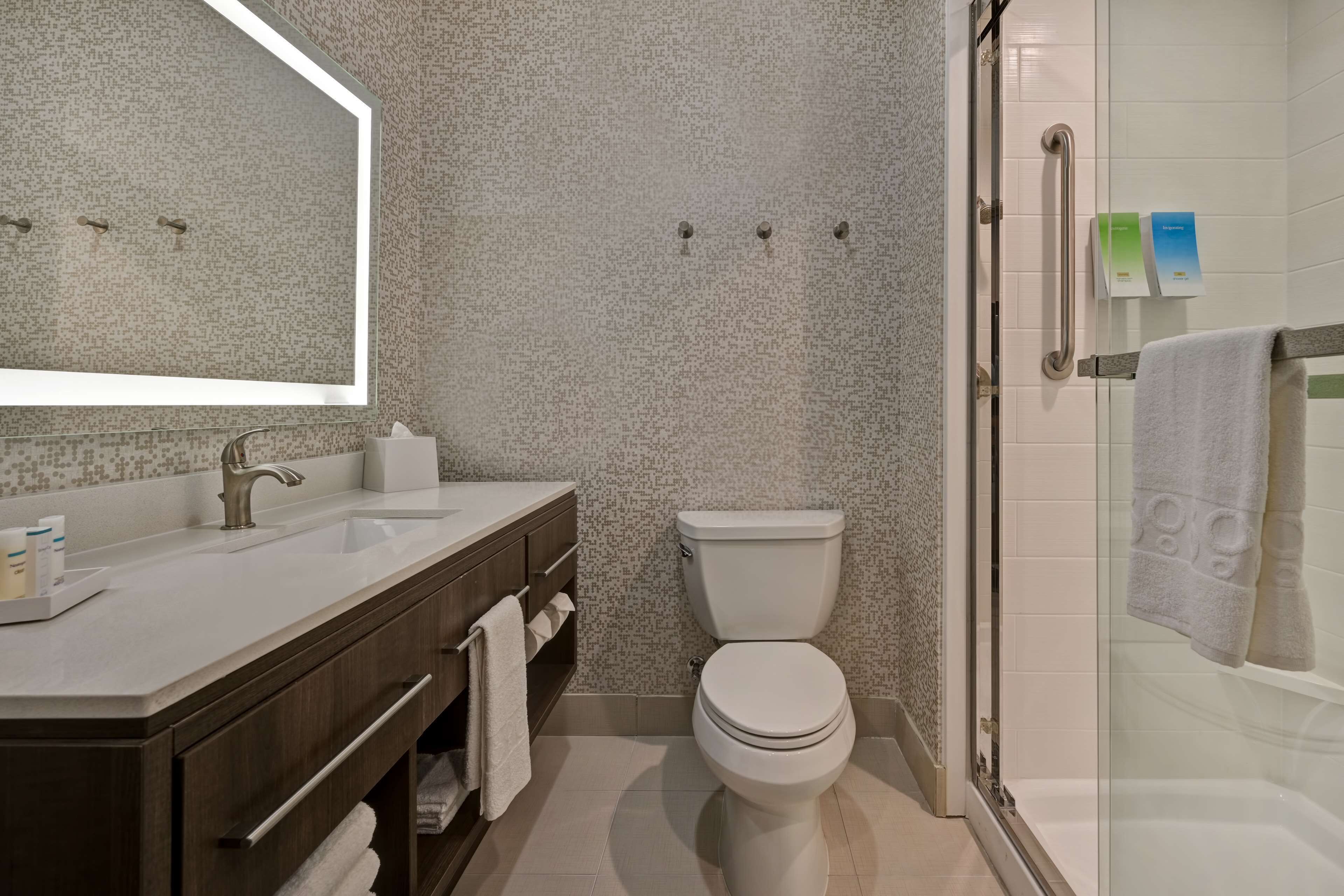 A modern bathroom with a large mirror, a sink, a toilet, and a glass-enclosed shower area.