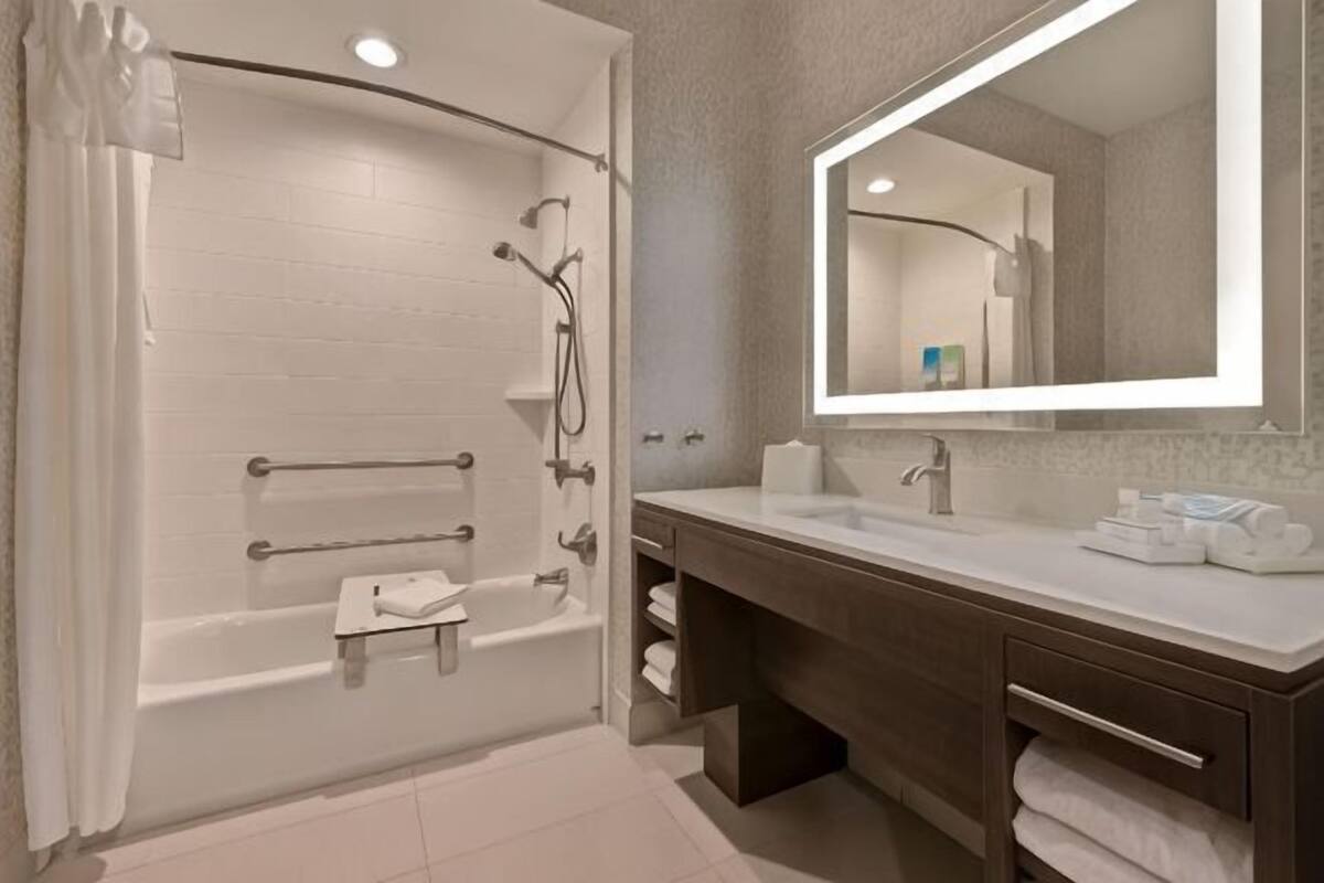 A modern bathroom with a bathtub, a sink, a mirror, and a towel rack.