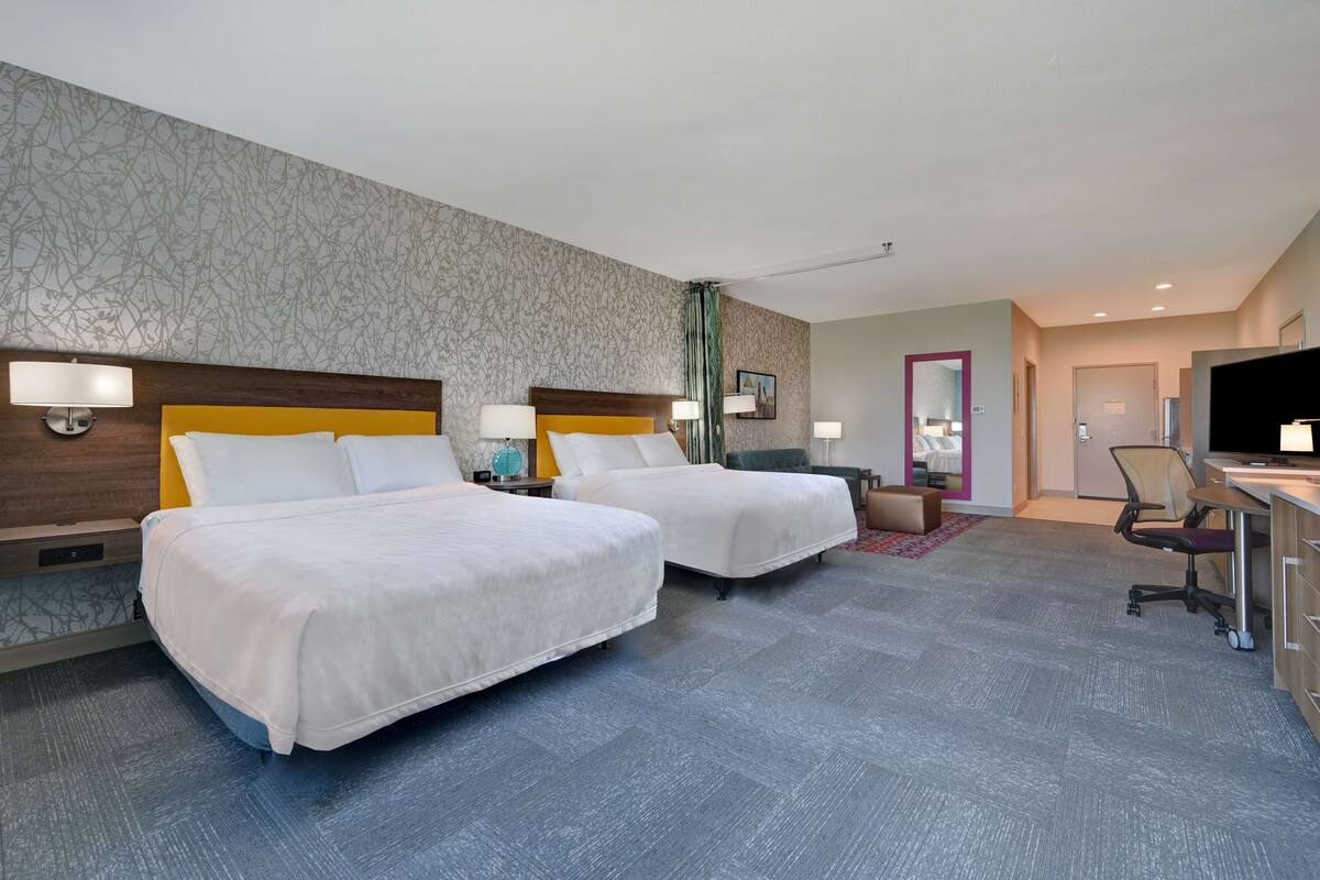 A hotel room with two beds, a desk, a chair, and a television.