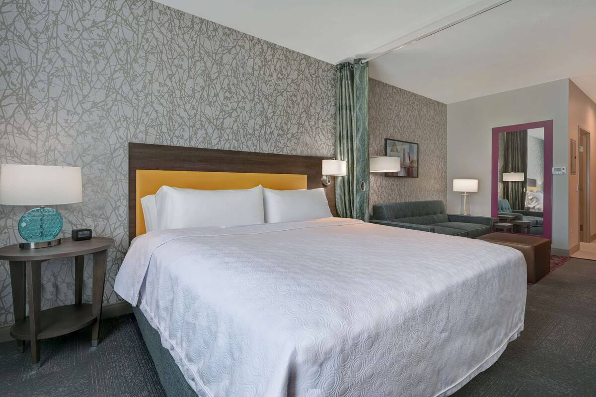 A hotel room with a large bed, a sofa, a small table, and a mirror.