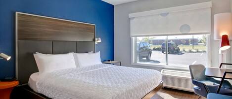 Quarto de hotel com uma cama grande, uma escrivaninha, uma cadeira, mesa de cabeceira e uma janela com vista para a rua.