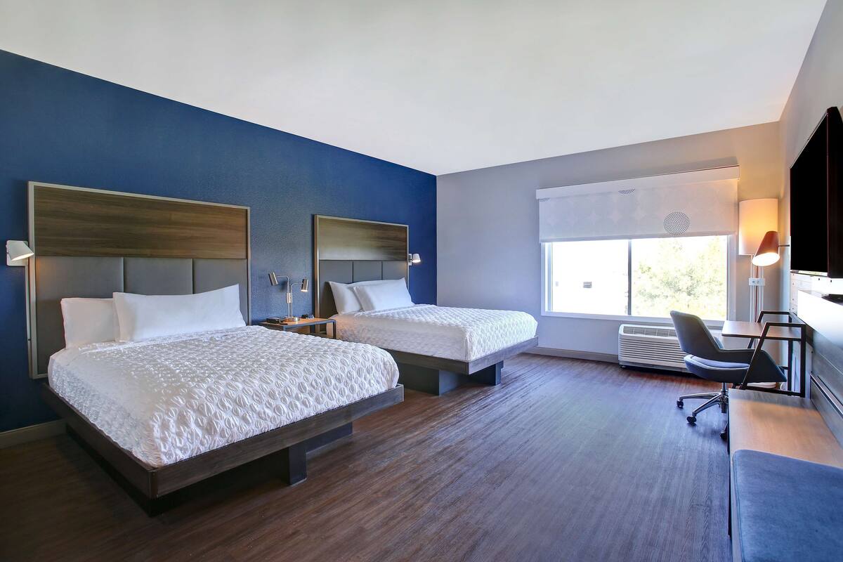 A hotel room with two beds, a desk, and a chair.