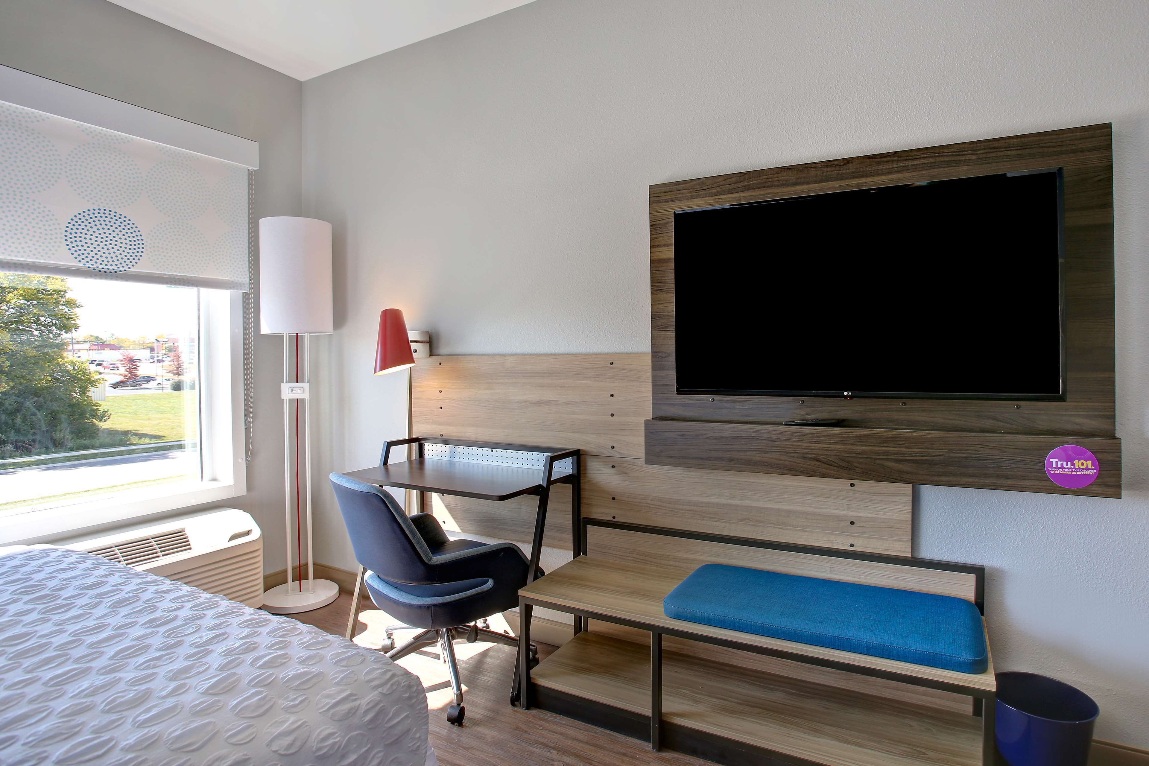 A hotel room with a bed, a desk, a chair, a TV, and a window with a view of the outdoors.