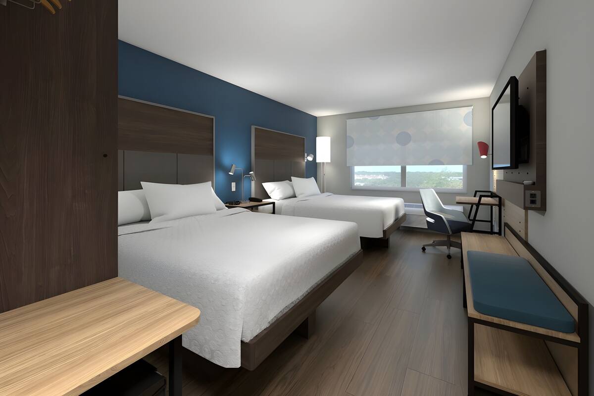 A hotel room with two beds, a desk, a chair, a TV, and a window with a view.