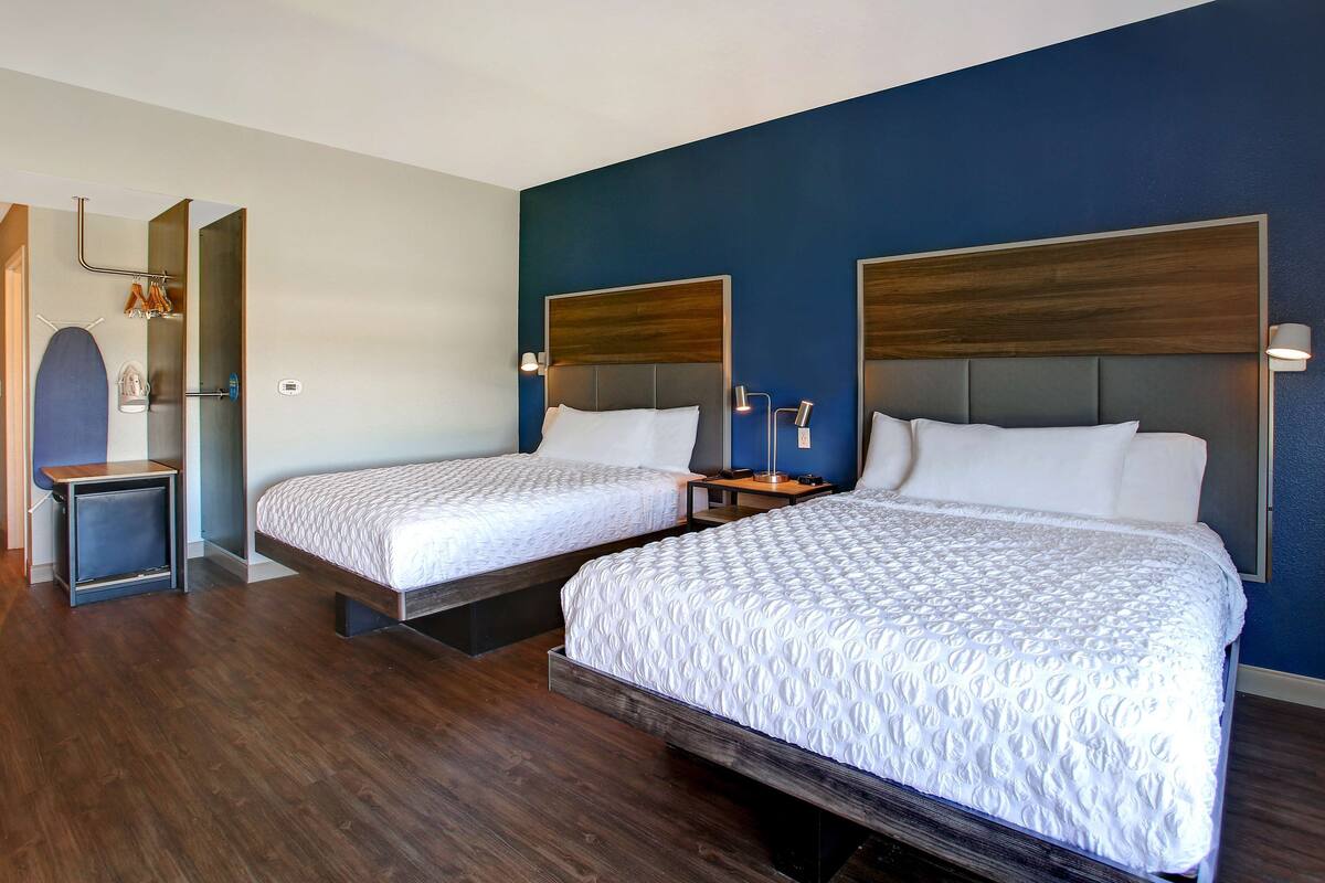 A hotel room with two beds, wooden flooring, and a dark blue accent wall.