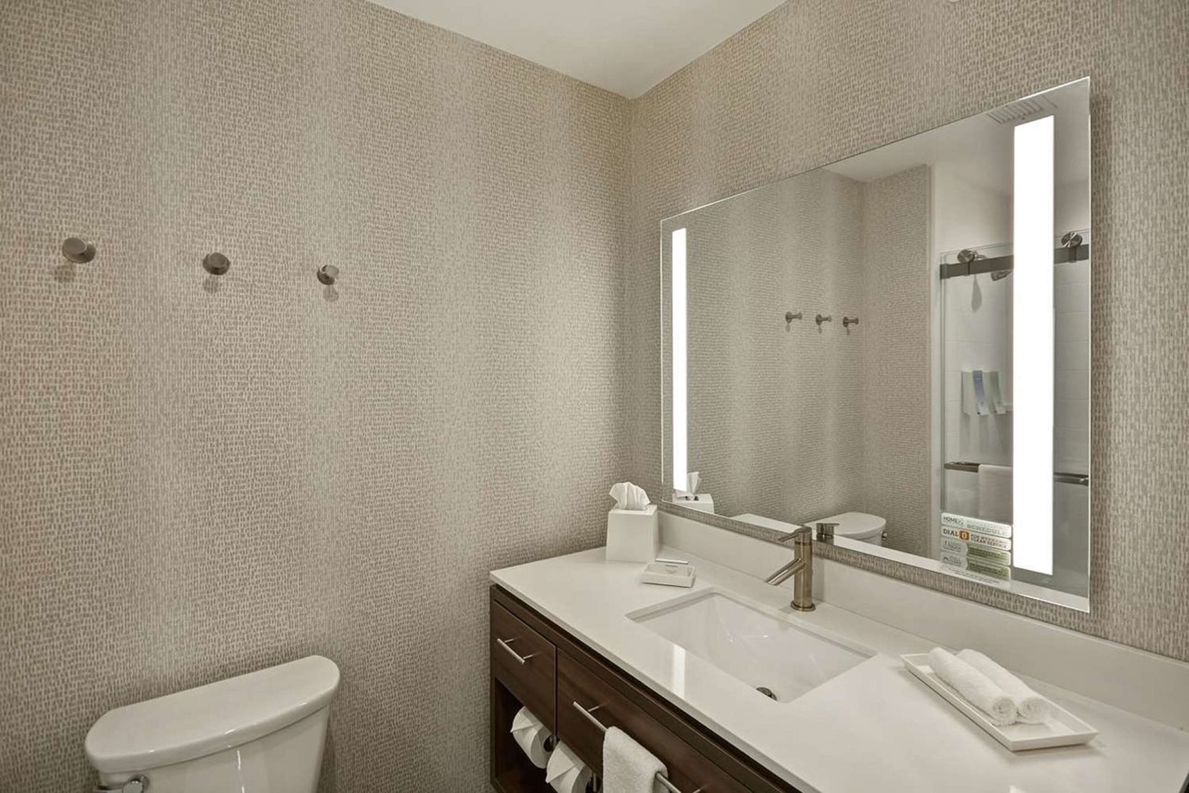 Un baño moderno con pared texturizada, un espejo grande, un lavabo blanco, un mueble de tocador de madera oscura y un inodoro.
