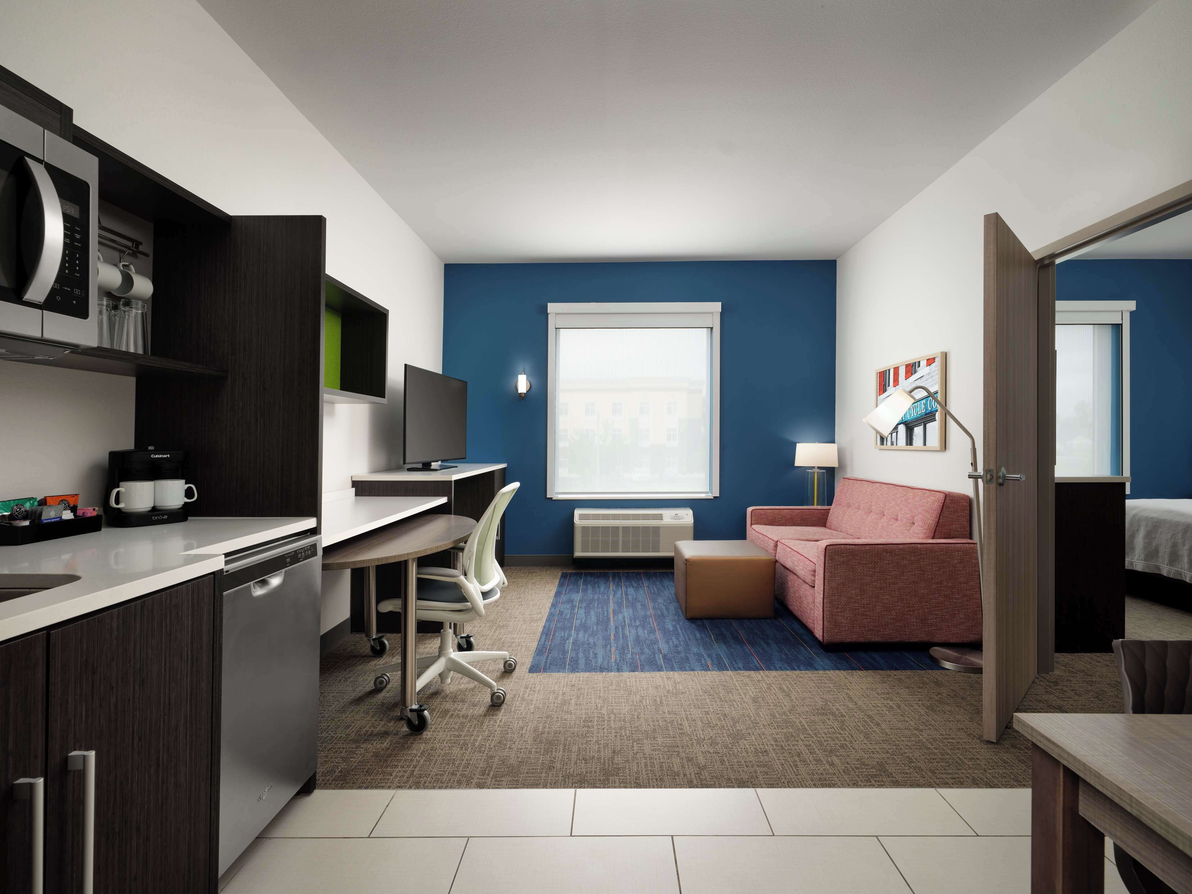 Una habitación de hotel compacta con kitchenette, un escritorio con silla, un sofá y una cama.