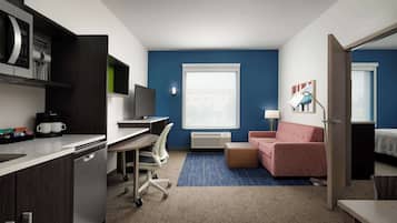 Una habitación de hotel compacta con kitchenette, un escritorio con silla, un sofá y una cama.