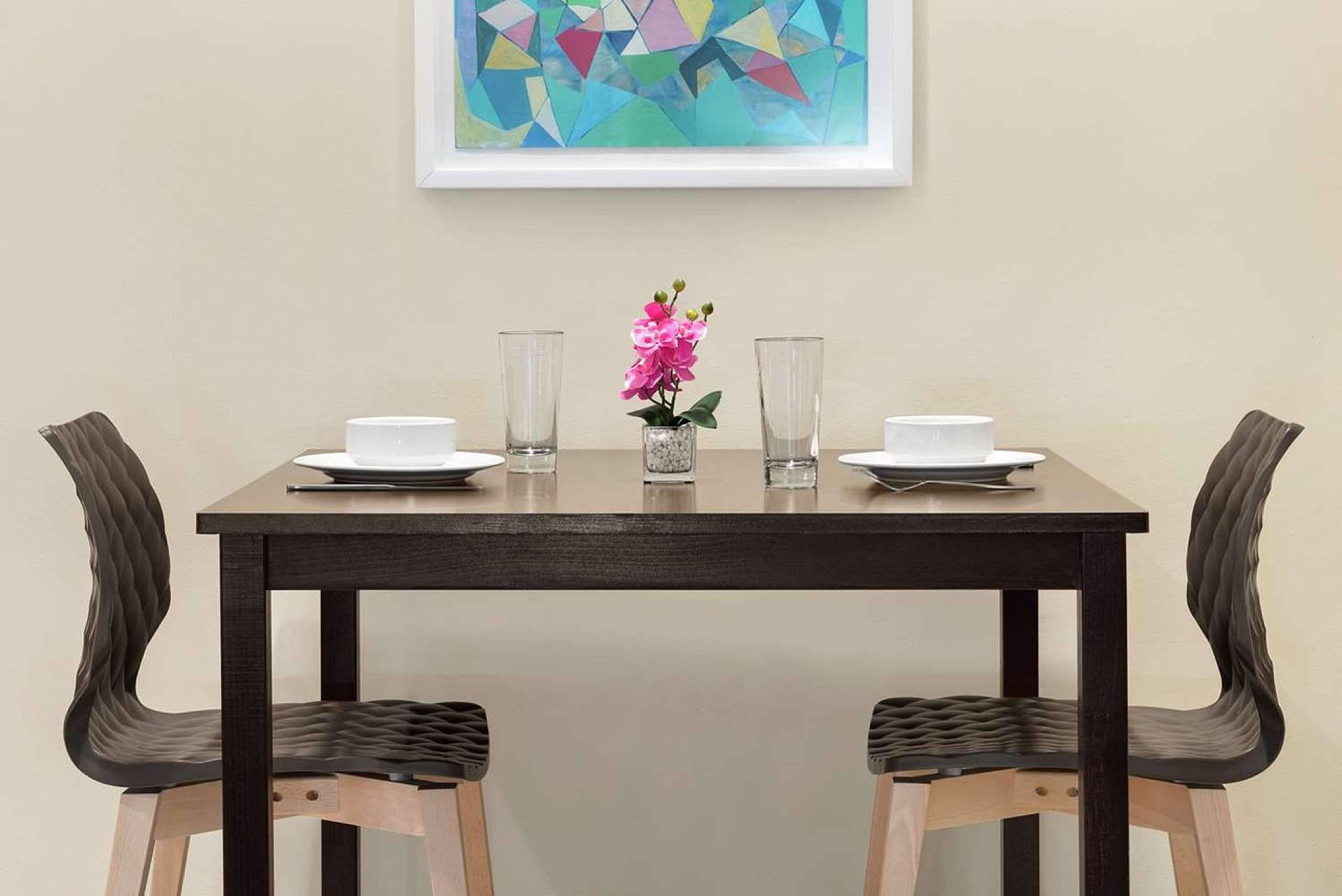A dining table with two chairs, a vase with flowers, and two glasses.