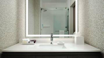 A modern bathroom with a large mirror, a white sink, dark wooden cabinets, and a shower visible in the reflection.