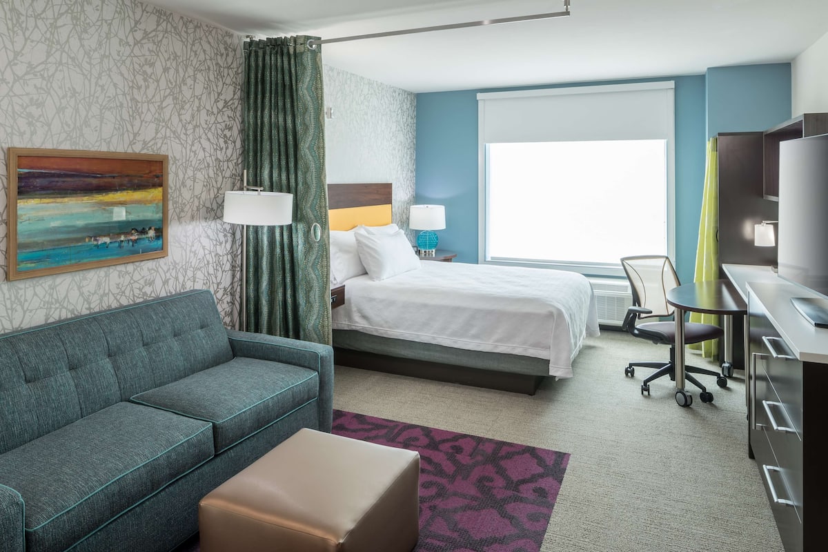 Ein Hotelzimmer mit Bett, Sofa, Schreibtisch, Fernseher und Fenster.