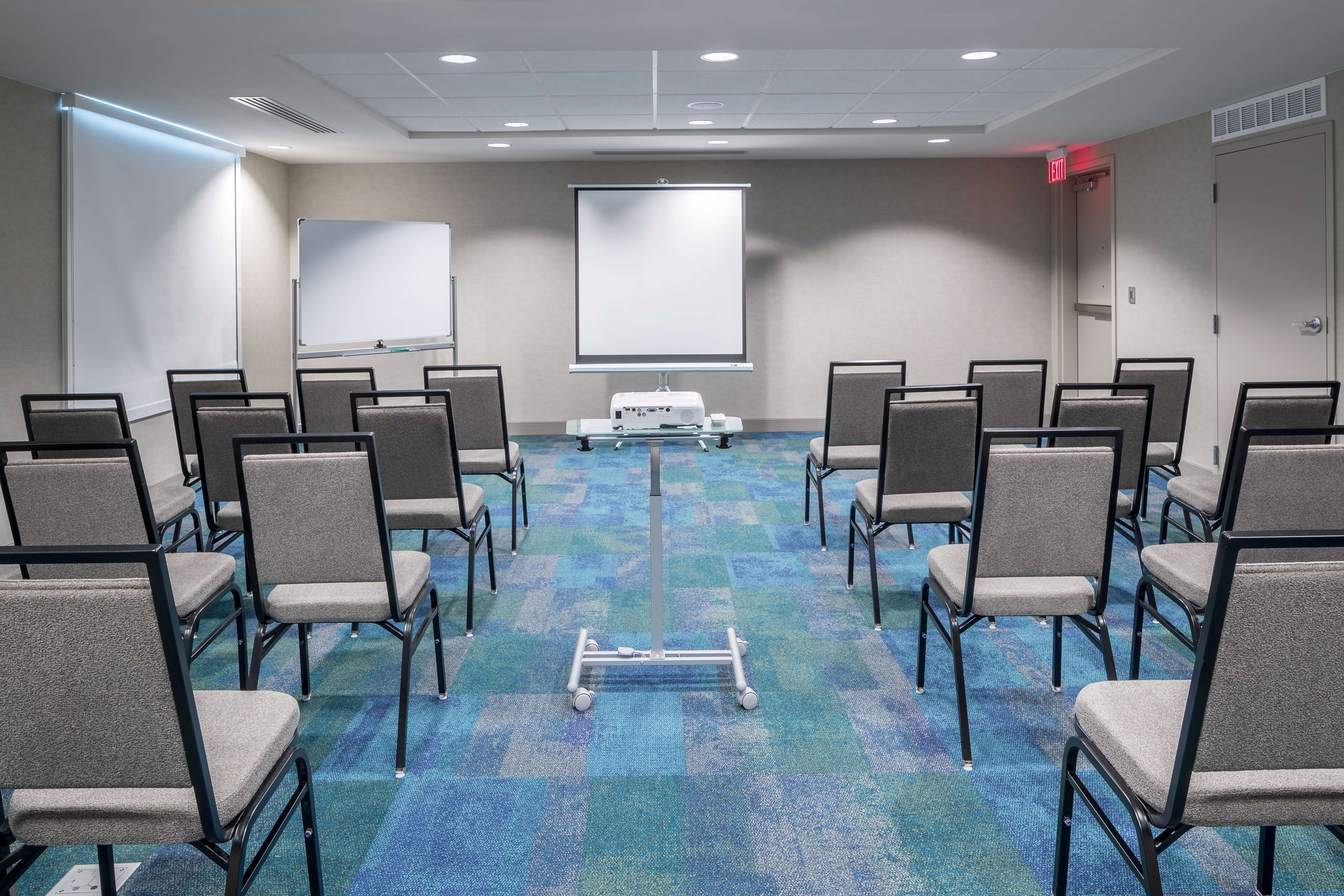 A conference room with rows of chairs, a projector screen, and a carpeted floor.