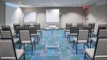 A conference room with rows of chairs, a projector screen, and a carpeted floor.