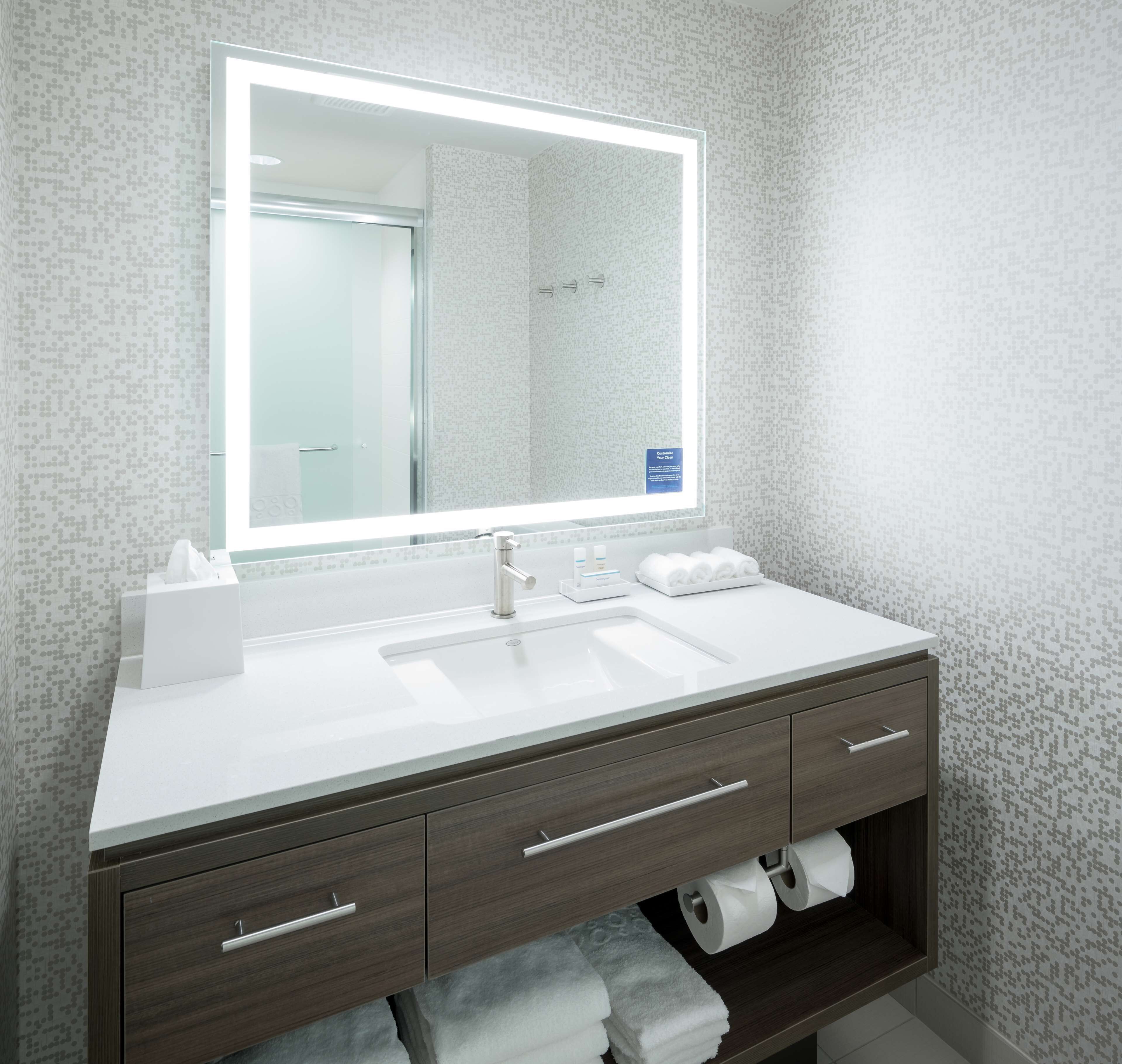 A modern bathroom with a large mirror, white sink, and dark wood vanity.
