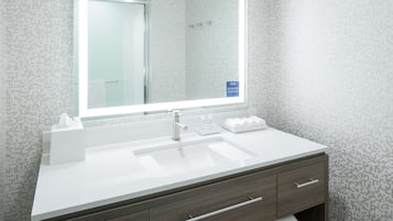 A modern bathroom with a large mirror, white sink, and dark wood vanity.