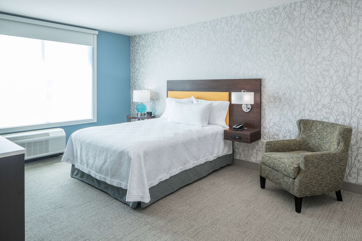 Ein Hotelzimmer mit Bett, Stuhl, Nachttisch und Fenster.