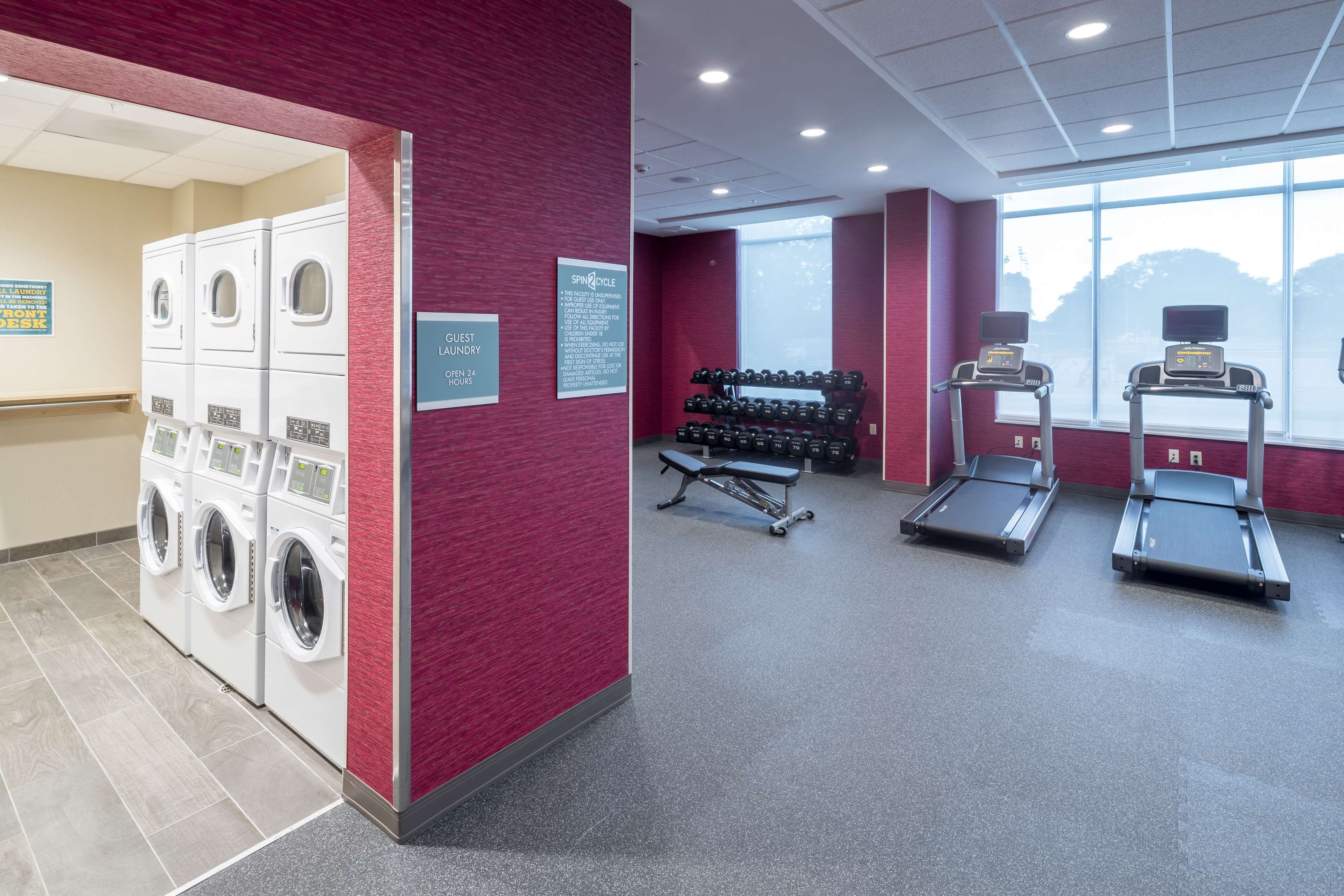 A laundry area with multiple washing machines, a guest lounge with a sign indicating open hours, and a fitness area with dumbbells and treadmills.