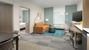A hotel room with a bed, a sofa, a desk, a chair, and a television.