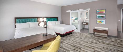 Ein Hotelzimmer mit zwei Betten, einem Schreibtisch, einem Stuhl, einem Spiegel und einer Tür zu einem Badezimmer.