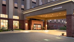 Een hotelentree met een 'Welcome'-bord, een heldere lucht en een parkeerplaats.