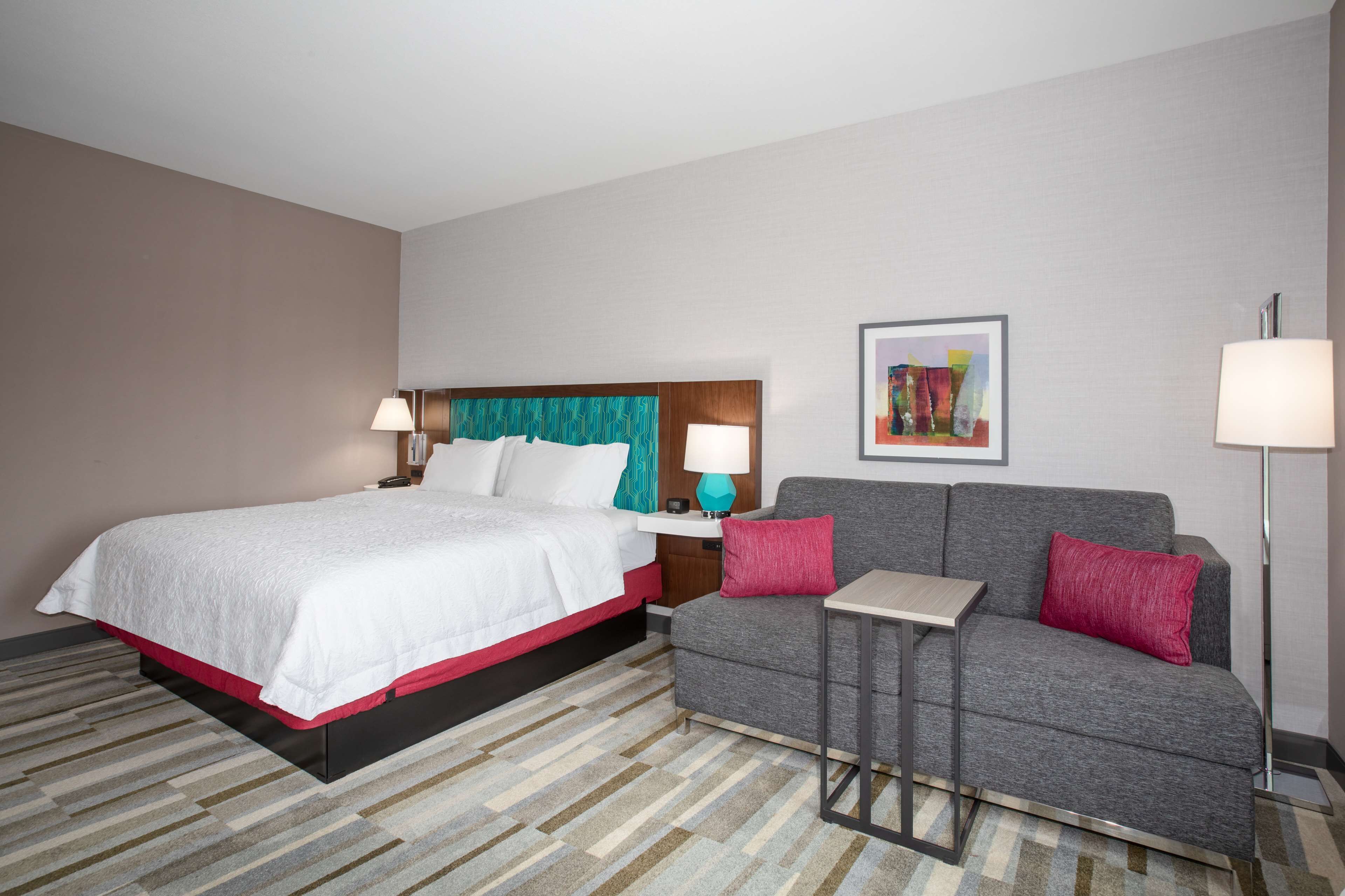 A hotel room with a bed, a sofa, a small table, and a lamp.