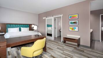 A hotel room with a bed, desk, chair, bedside table, and artwork on the wall.