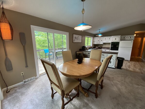 A dining area with a wooden table and chairs, a hanging light fixture, and a view of a deck with outdoor furniture.