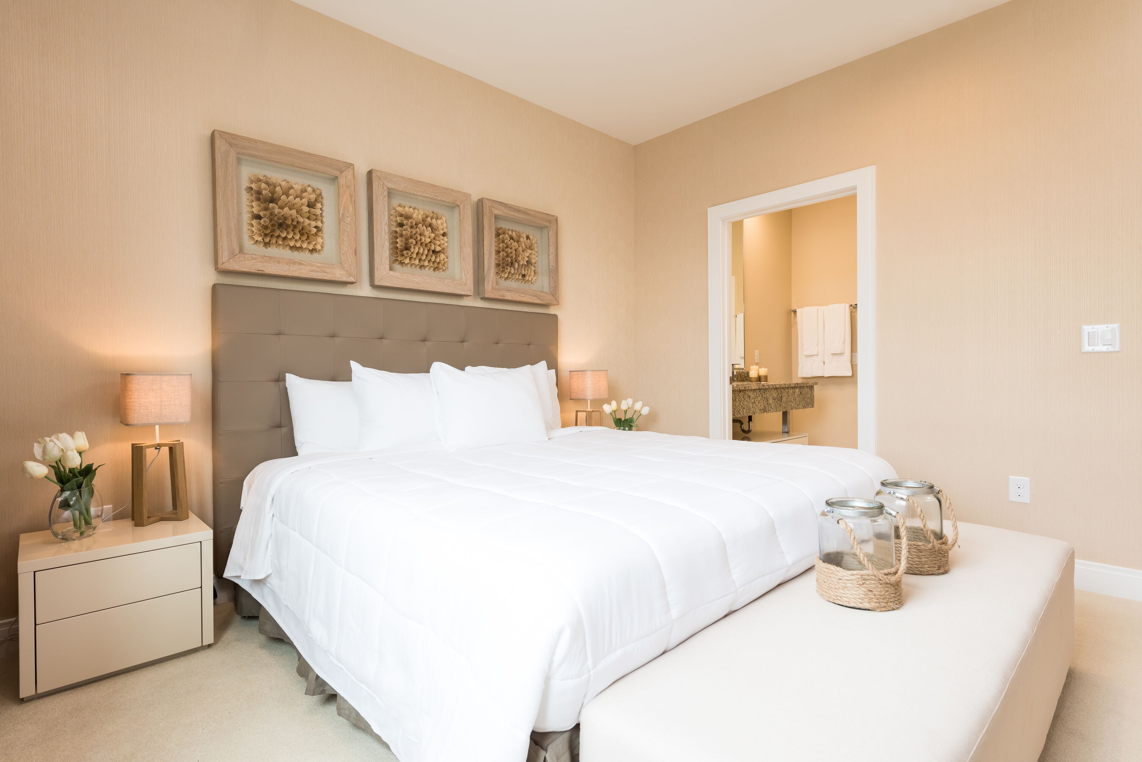 Une chambre à coucher bien aménagée, avec un grand lit, des tables de chevet avec des lampes et des œuvres d’art décoratives au mur.