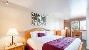Een hotelkamer met een groot bed, twee nachtkastjes met lampen, een houten hoofdeinde, een kunstwerk aan de muur, een bureau met stoel, en een raam met gordijnen.