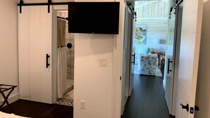 Una habitación con puerta corrediza que da a un balcón, televisor de pantalla plana montado en la pared y baño con cortina de ducha.