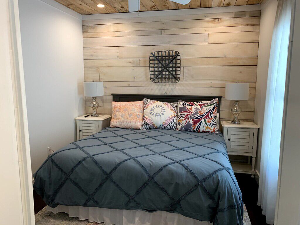 Una camera da letto con soffitto in legno, un letto con copriletto blu e due comodini con lampade.