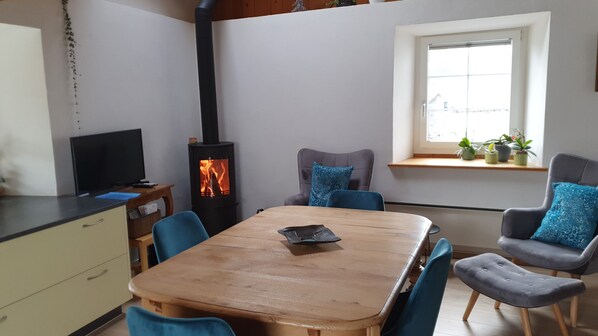 Una sala de estar acogedora con una mesa de madera, sillas azules, un televisor y un estufa de leña.