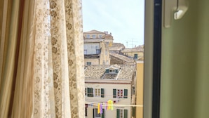 A view from a window with lace curtains, overlooking a row of buildings with tiled roofs and balconies. - Anesis Studio Old Corfu Town (Corfu)