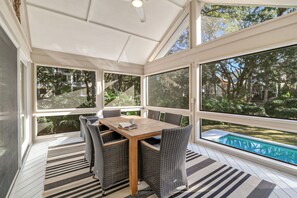 A covered outdoor dining area with a wooden table and wicker chairs, large windows, and a view of a swimming pool. - Pet friendly, 2nd row beach home with private pool and gorgeous new updates (Hilton Head Island)