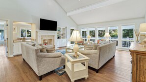 Ein geräumiges Wohnzimmer mit zwei Sofas, einem Kamin, einem Fernseher und großen Fenstern mit Blick ins Freie.