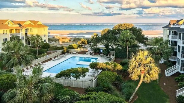Une propriété située en bord de mer, dotée d’une piscine, de palmiers et offrant une vue sur l’océan.