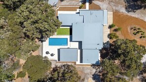 An aerial view of a modern house with a swimming pool, a covered patio, and a well-maintained lawn.