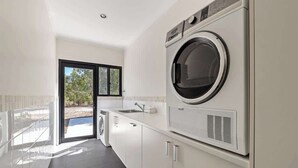 Un espace buanderie comprenant un lave-linge, un sèche-linge, un évier et une porte donnant sur l’extérieur.