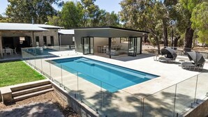 Un espace piscine extérieur moderne doté d’un patio vitré et de mobilier d’extérieur.