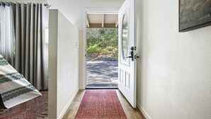 A hallway leading to a door with a view of a road and greenery outside.