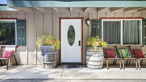 A house with a front door, two large barrels as planters, and a porch with four chairs.