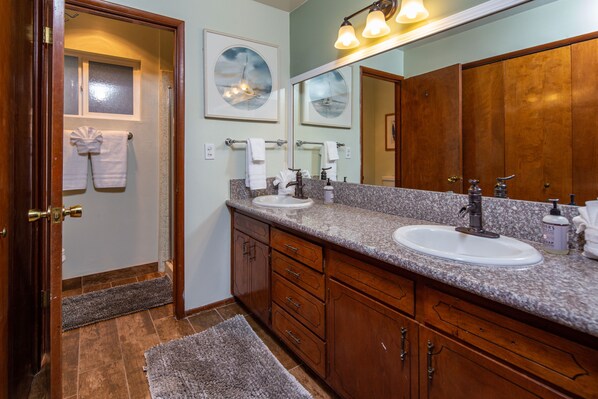 A bathroom with two sinks, wooden cabinets, a large mirror, and artwork on the wall.