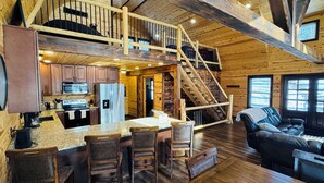 A spacious cabin interior with a kitchen, dining area, and a staircase leading to an upper level. - Beautiful Cabin on 20 Acres in Hocking Hills Ohio - Early Bird Discounts! (Rockbridge)