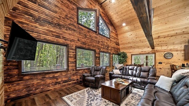 A spacious living room with a wooden interior, leather furniture, and large windows offering views of greenery. - Beautiful Cabin on 20 Acres in Hocking Hills Ohio - Early Bird Discounts! (Rockbridge)