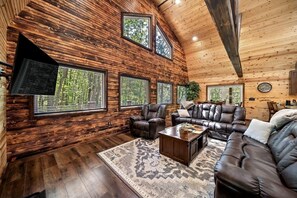 A spacious living room with a wooden interior, leather furniture, and large windows offering views of greenery. - Beautiful Cabin on 20 Acres in Hocking Hills Ohio - Early Bird Discounts! (Rockbridge)
