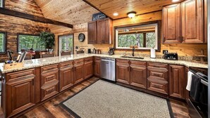 A spacious kitchen with wooden cabinets, granite countertops, and a built-in dishwasher. - Beautiful Cabin on 20 Acres in Hocking Hills Ohio - Early Bird Discounts! (Rockbridge)