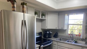 A modern kitchen with stainless steel appliances, a coffee maker, and a window with a view of trees. - Orlando Spacious Home Near Universal (Orlando)