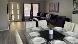 A dining area with a glass table set for six, a dark brown sofa, and a painting on the wall. - Orlando Spacious Home Near Universal (Orlando)